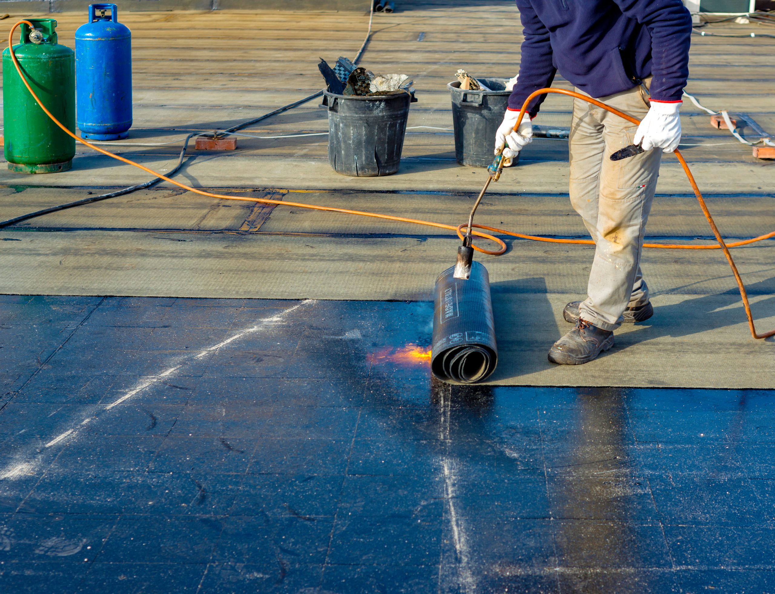 Worker preparing part of bitumen roofing felt roll for melting by gas heater torch flame